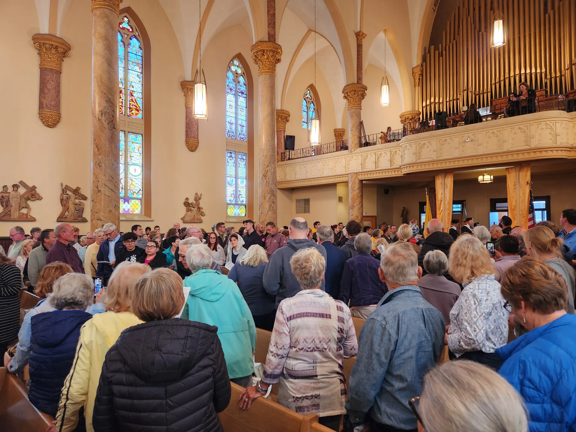 Interior of a church. The worshipers have their backs turned to the back of the church waiting for the procession to enter