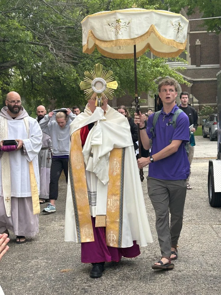 Bishop carries the Monstrance, while a young man carries an ombrellino