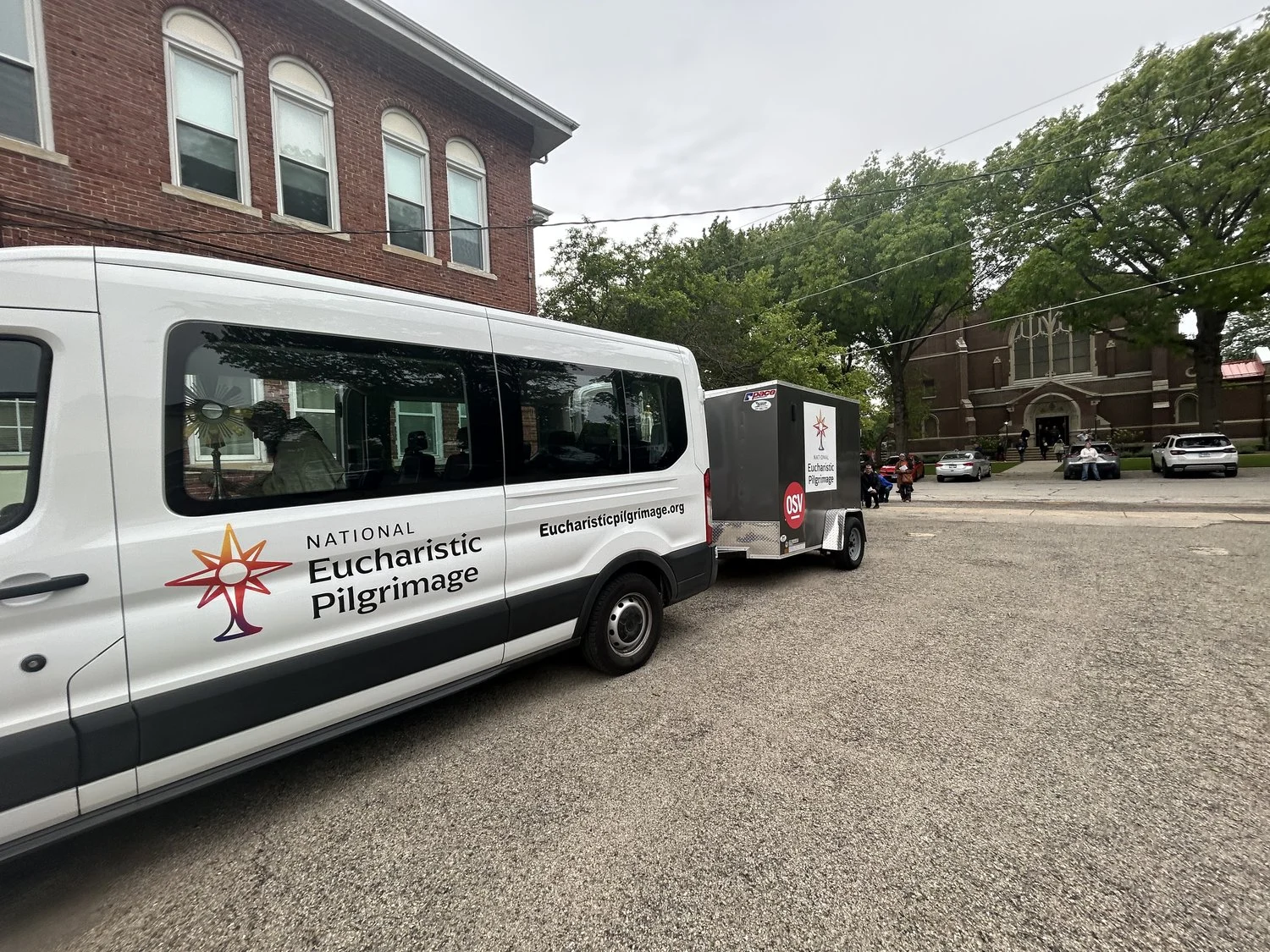 A white van pulling a trailer. Both include a logo that reads "National Eucharistic Pilgrimage"
