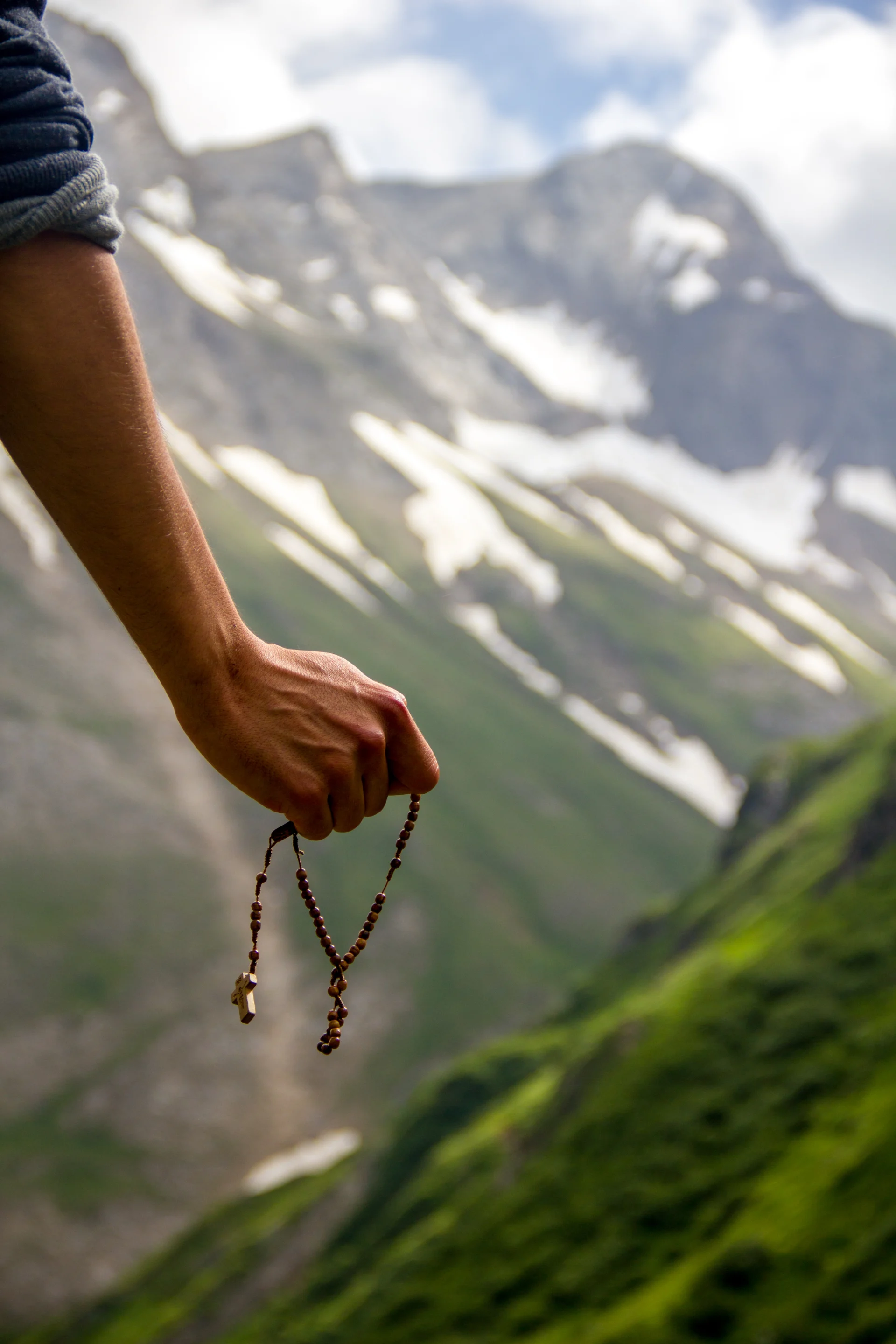 A man holding a rosary in front of mountains